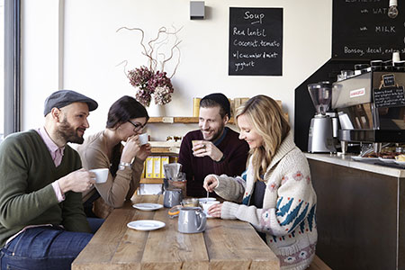 Four friends sitting and smiling in coffee shop while talking. Learn CBT to beat social anxiety.