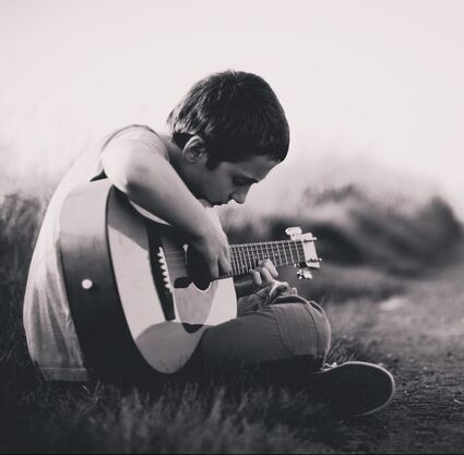 Boy plays guitar while seated on the grass in an open field. Anxiety disrupts daily life, and in therapy children find new ways to cope. 