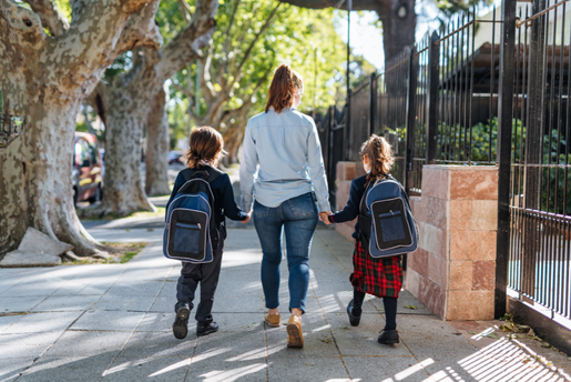 Mother holds hands with two children and walks them to school. Parents can help their children learn tools to feel confident about returning to school after a long break.