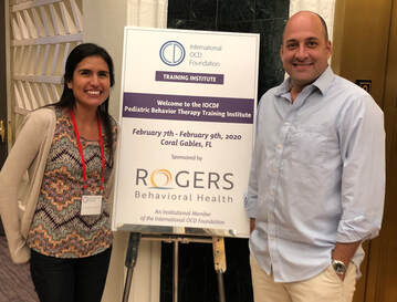 Dr. Eli Penela stands with Dr. Eric Storch near a sign announcing the IOCDF Behavior Therapy Training Institute (BTTI)