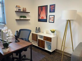 Brown desk, black office chair, and colorful photos frames inside Dr. Penela’s office. Tele-health therapy services provided throughout Florida 
