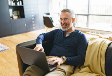 Hombre sonriente sentado en un sofá, mirando la pantalla de su computadora. Tratamiento para el TOC y la ansiedad se puede hacer de manera efectiva online. 